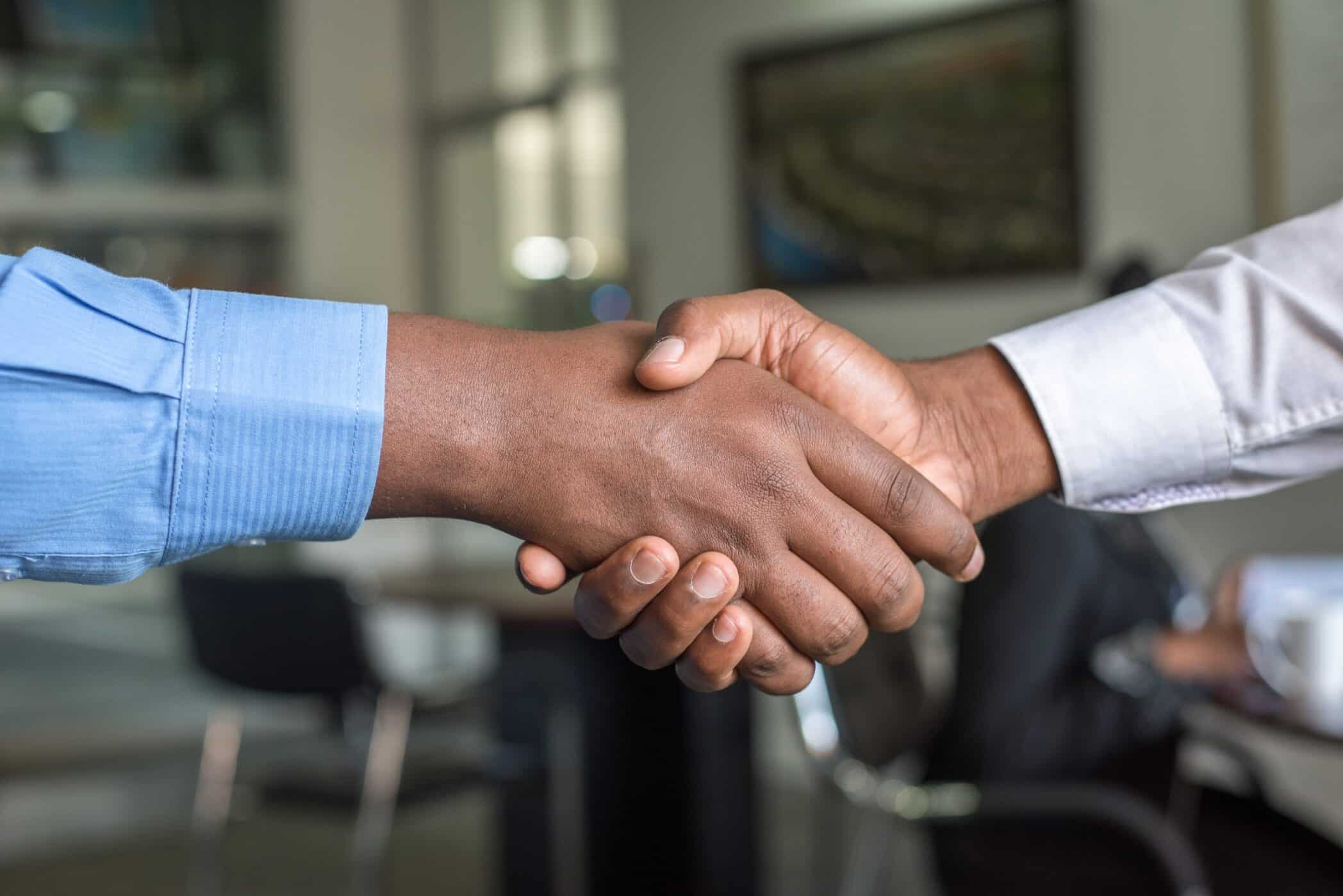 A close up photo of two men's hands clasped together in a handshake.