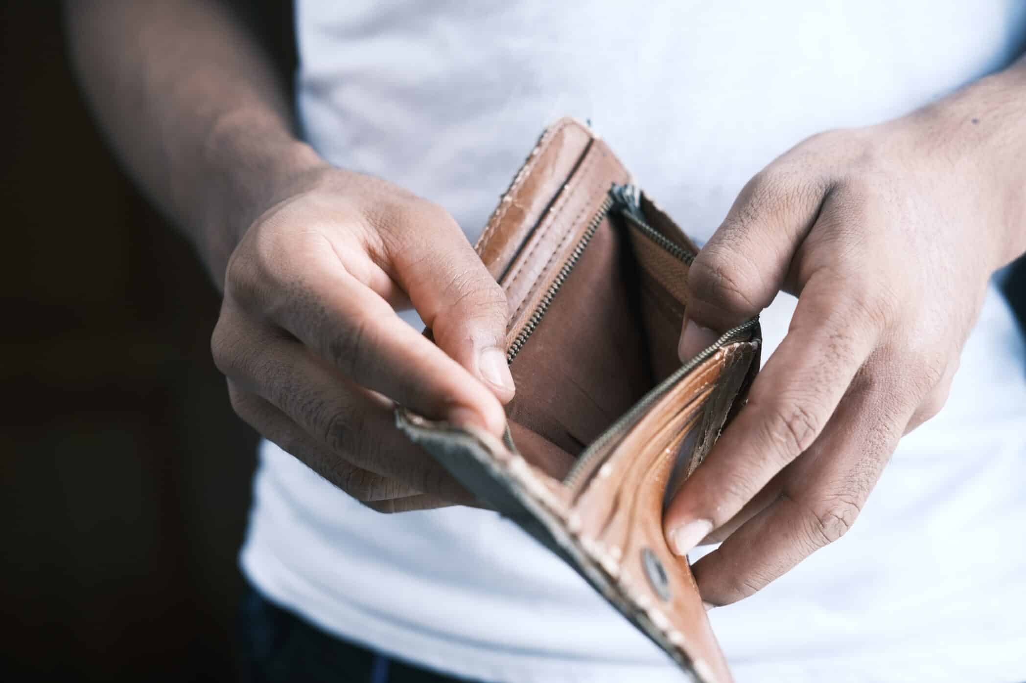 A person is holding open an empty brown wallet